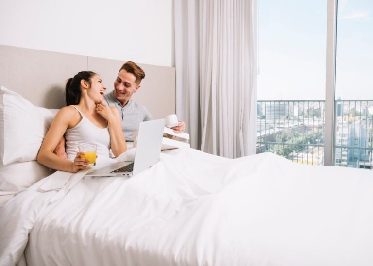 a happy couple cuddling in bed with drinks and a laptop