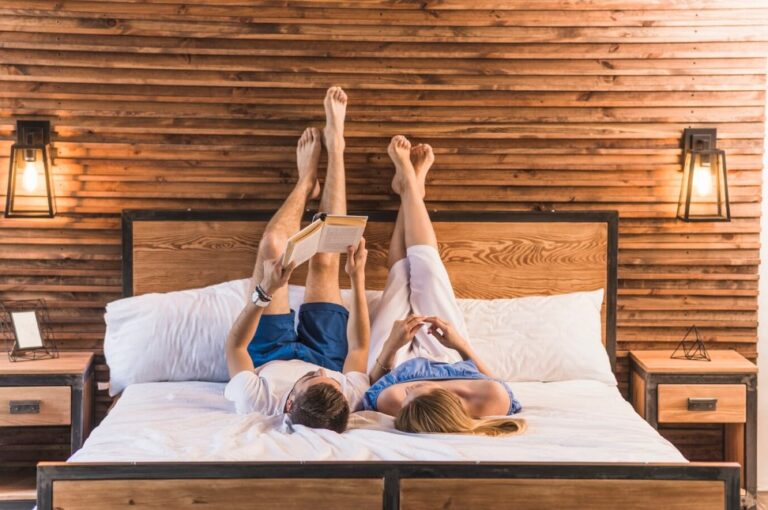 a couple lying on a cozy bed with their legs up on the wall