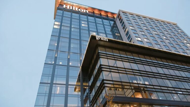 Exterior view of a modern Hilton hotel building with the logo illuminated at twilight