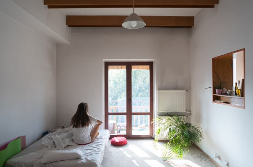 Woman sitting on bed looking out the balcony door in a bright room