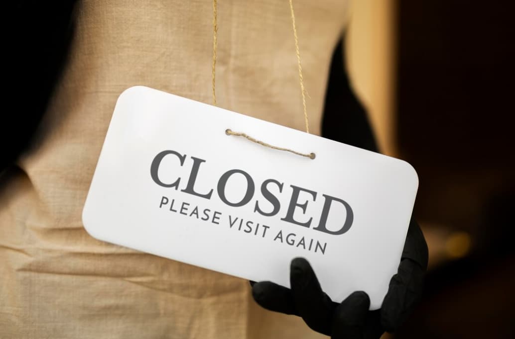 A person in a suit holding a "CLOSED" sign, indicating the closure of a business