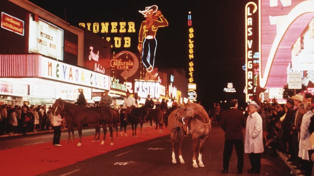 Vintage photo of a crowded Las Vegas street with neon signs and horseback riders