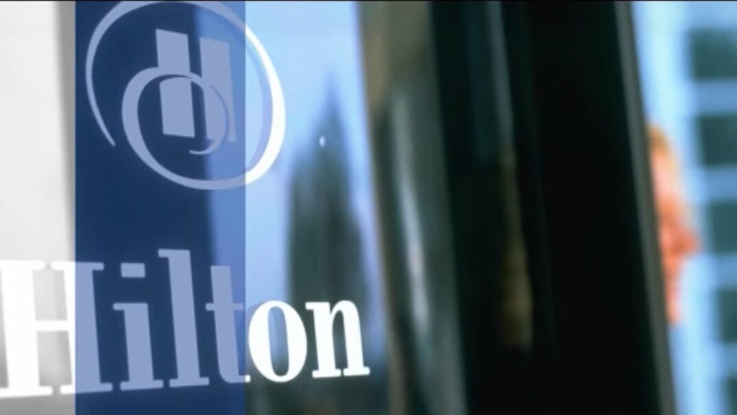 the Hilton logo on a glass surface with reflections of the surrounding architecture